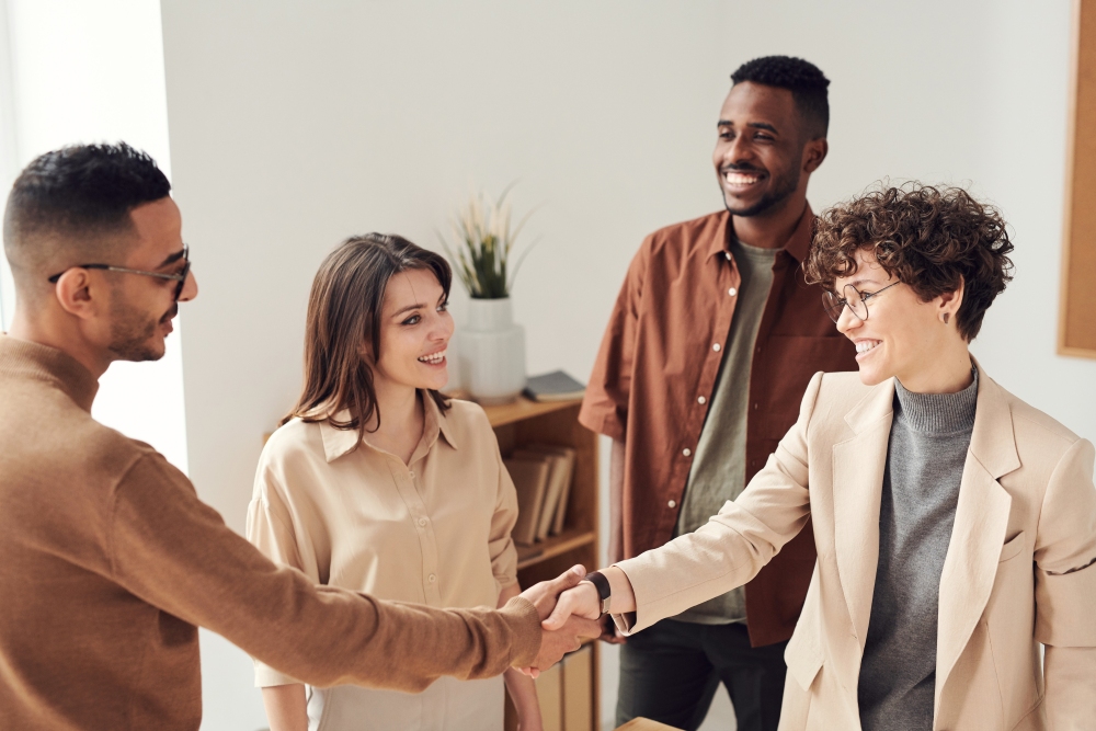 4 people smiling and standing. 2 of them shaking hands